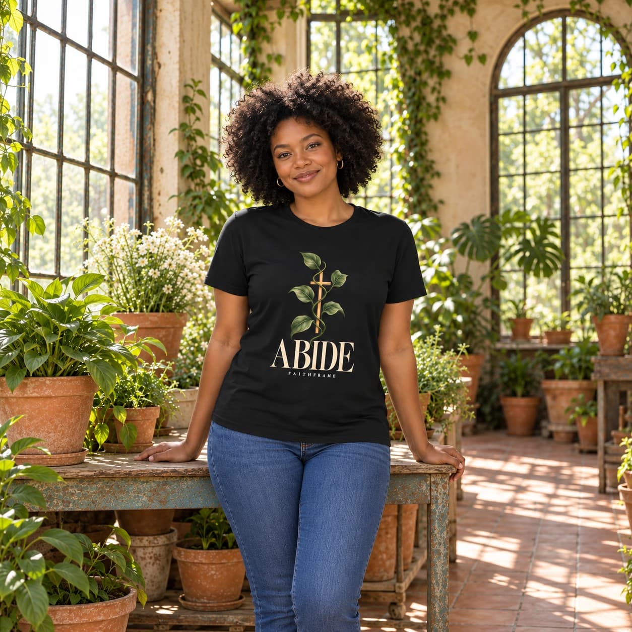 Woman wearing the black Abide tee in a sunlit plant conservatory