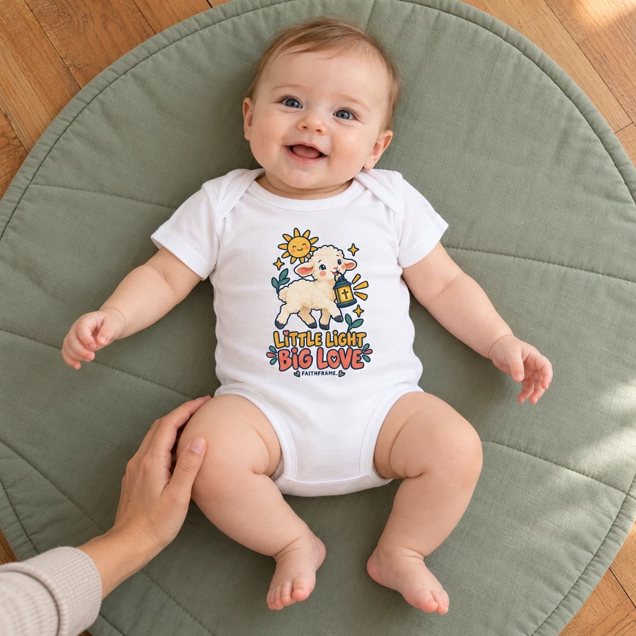 Baby wearing the white Little Light Big Love bodysuit on a floor play mat beside a caregiver