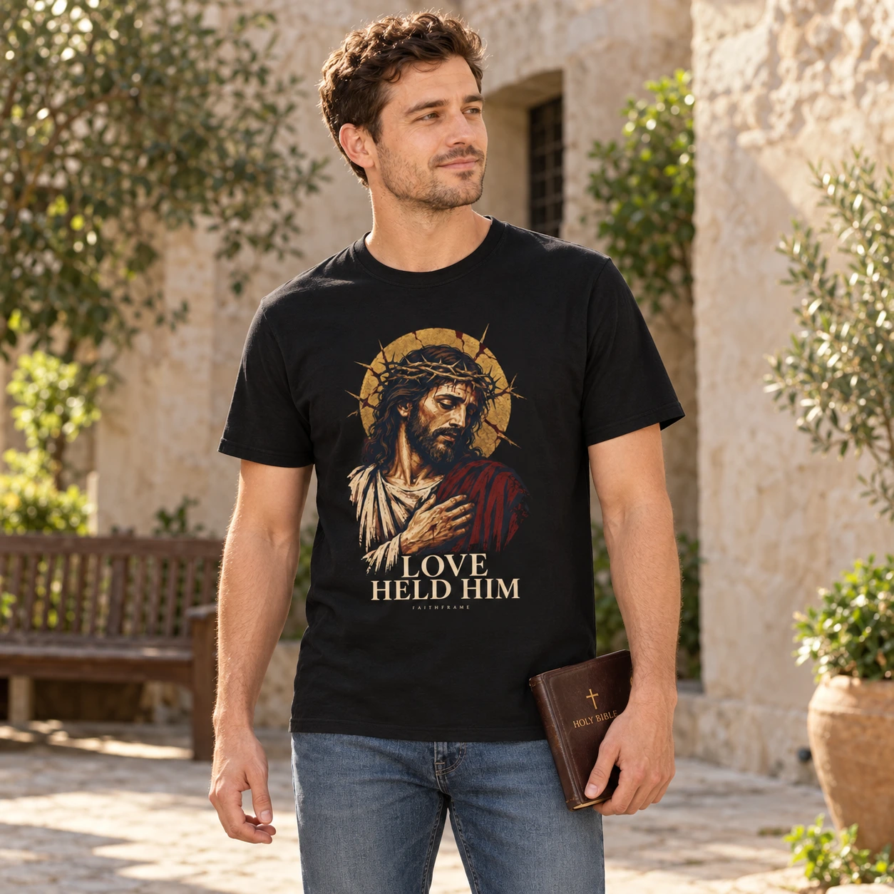 Man wearing the black Love Held Him tee in a sunlit courtyard, carrying a Bible at his side